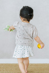Toddler walking with flower and orange while wearing Avauma Buttercumin sand floral cardigan.